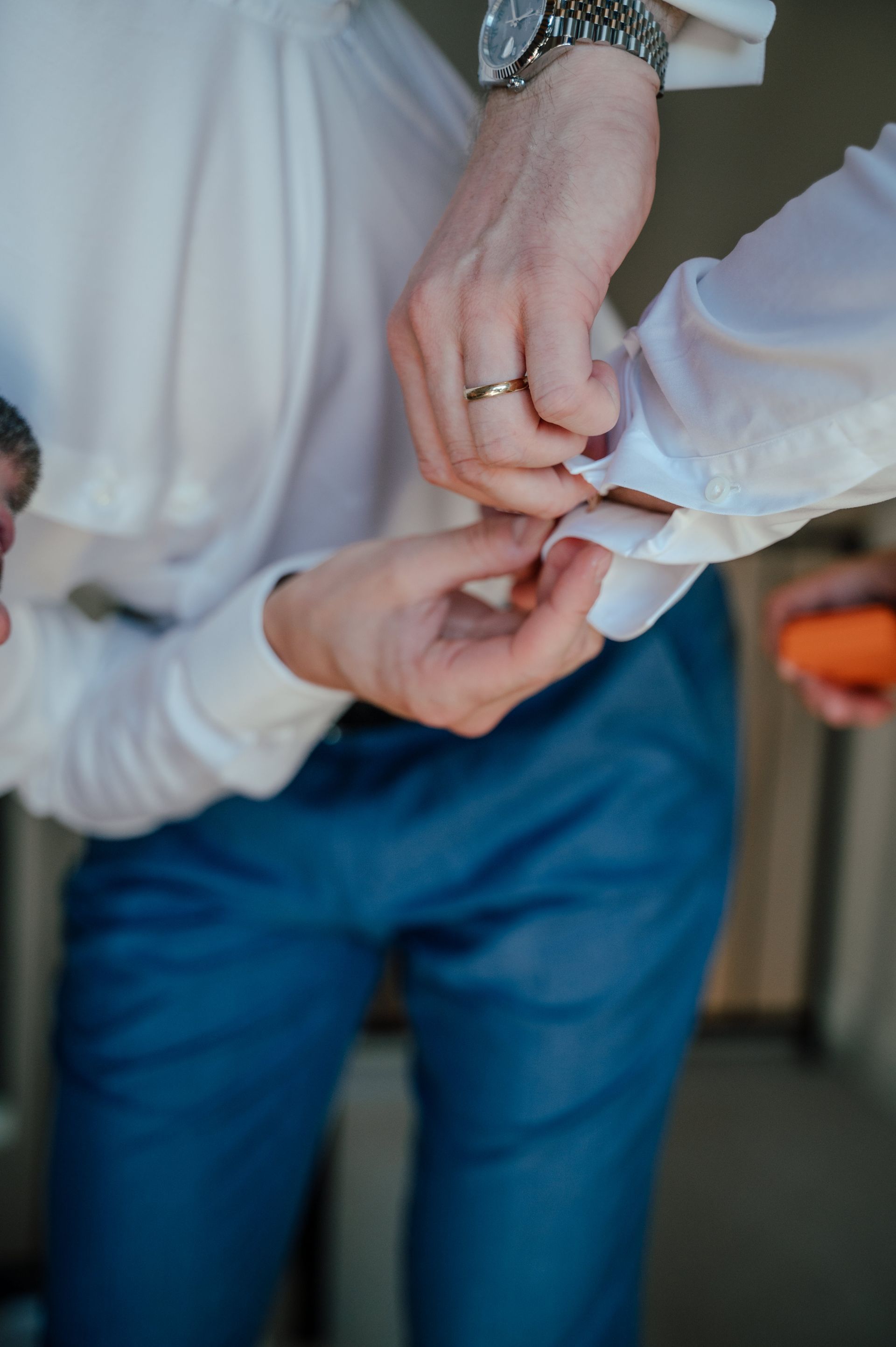A person wearing a white shirt and blue pants is adjusting the cuff of their sleeve.