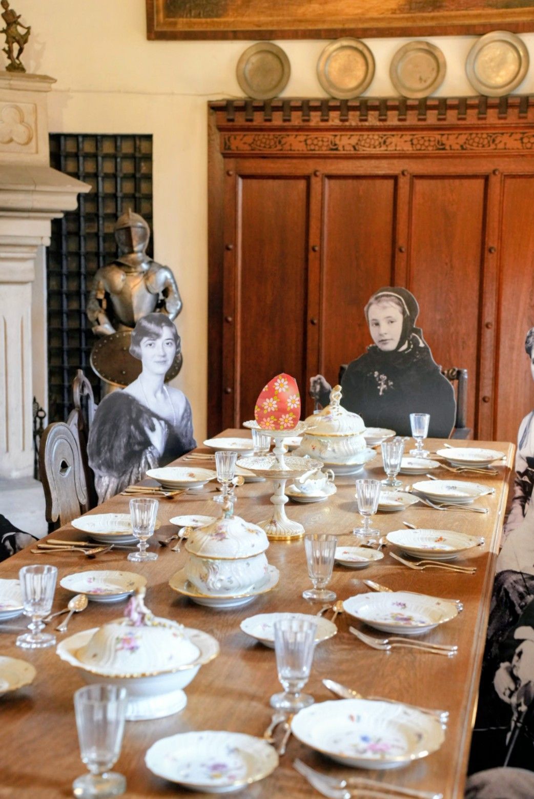 In einem historischen Raum mit Holzvertäfelung, Ziertellern und einer Rüstung ist ein Esstisch mit Porzellan gedeckt.