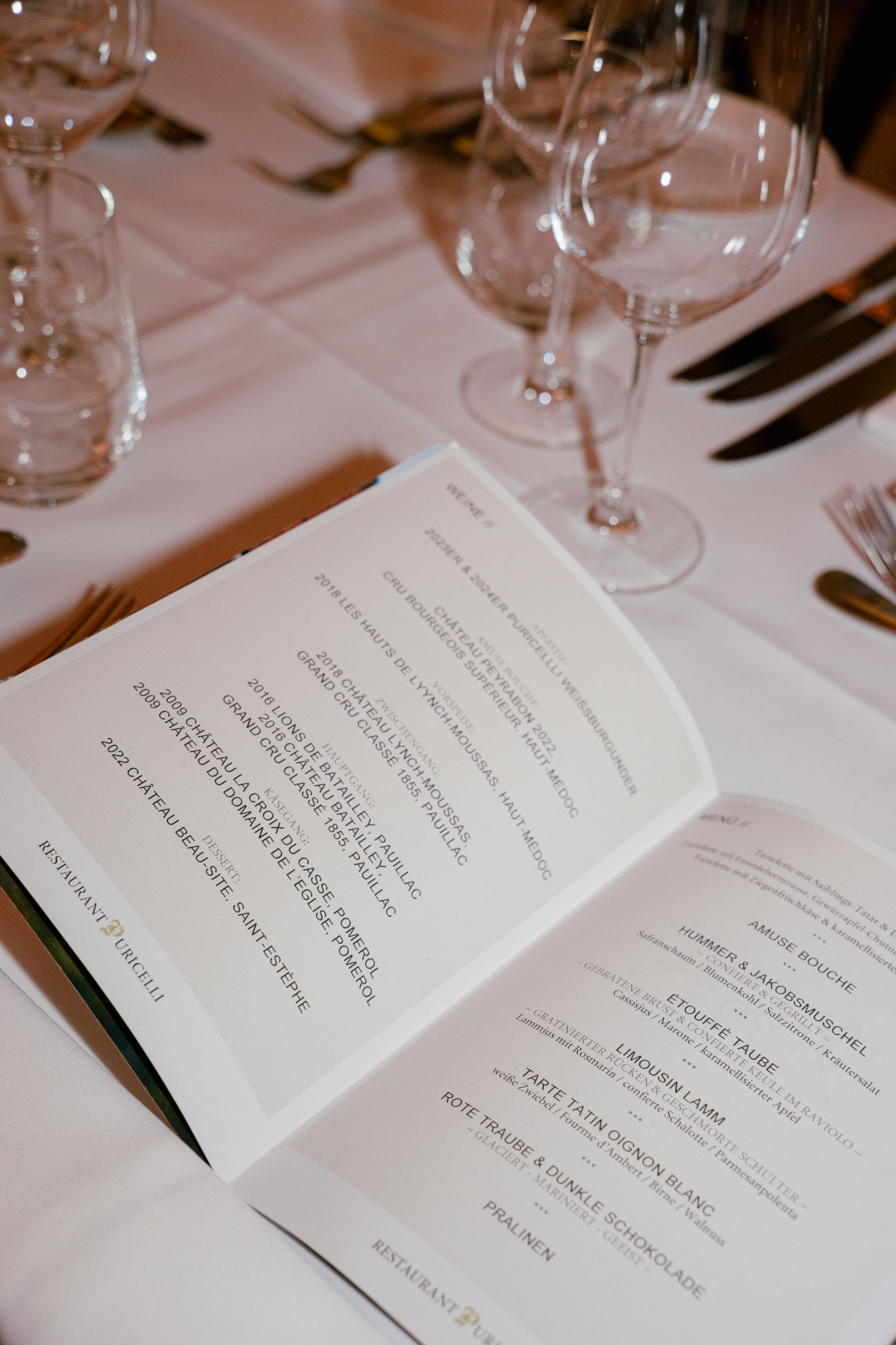Ein aufgeschlagenes Noten- oder Gedichtbuch liegt auf einem festlich gedeckten Esstisch mit Weingläsern und Silberbesteck.
