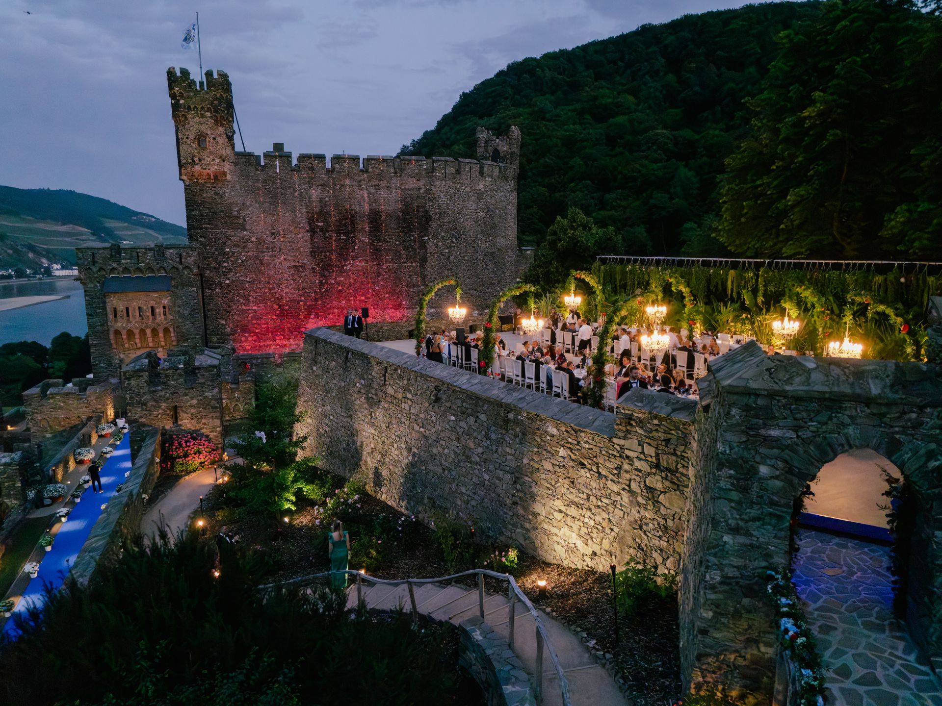 An evening event featuring dining tables lit by chandeliers within the stone walls of a historic castle.