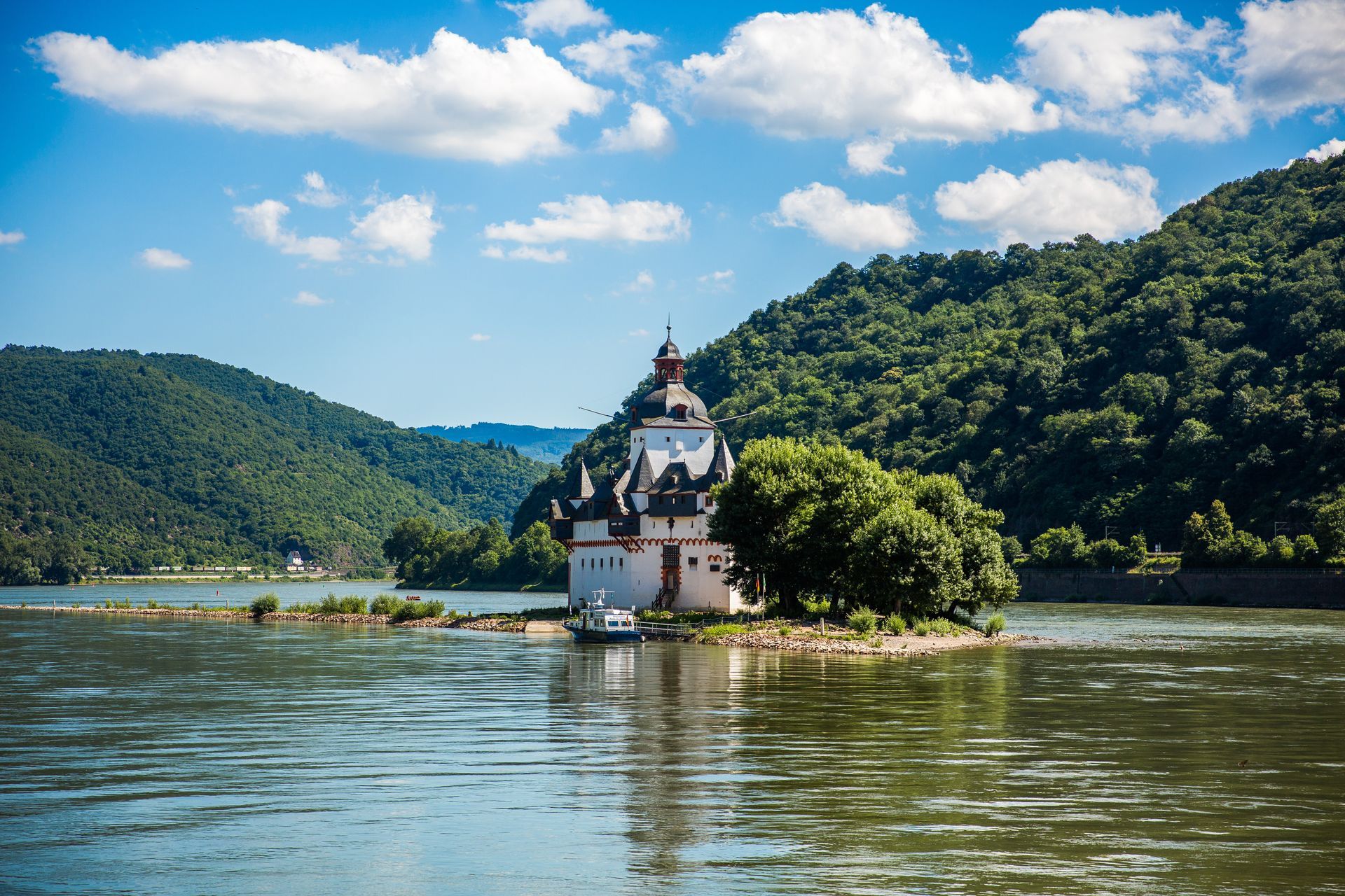 Schloss Pfalzgrafenstein auf einer kleinen Insel im Rhein, umgeben von grünen Hügeln unter einem teilweise bewölkten Himmel.