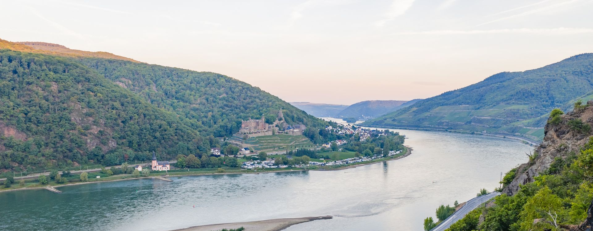 Weitwinkelaufnahme eines Flusses, der bei Sonnenuntergang durch ein üppig grünes Bergtal fließt.