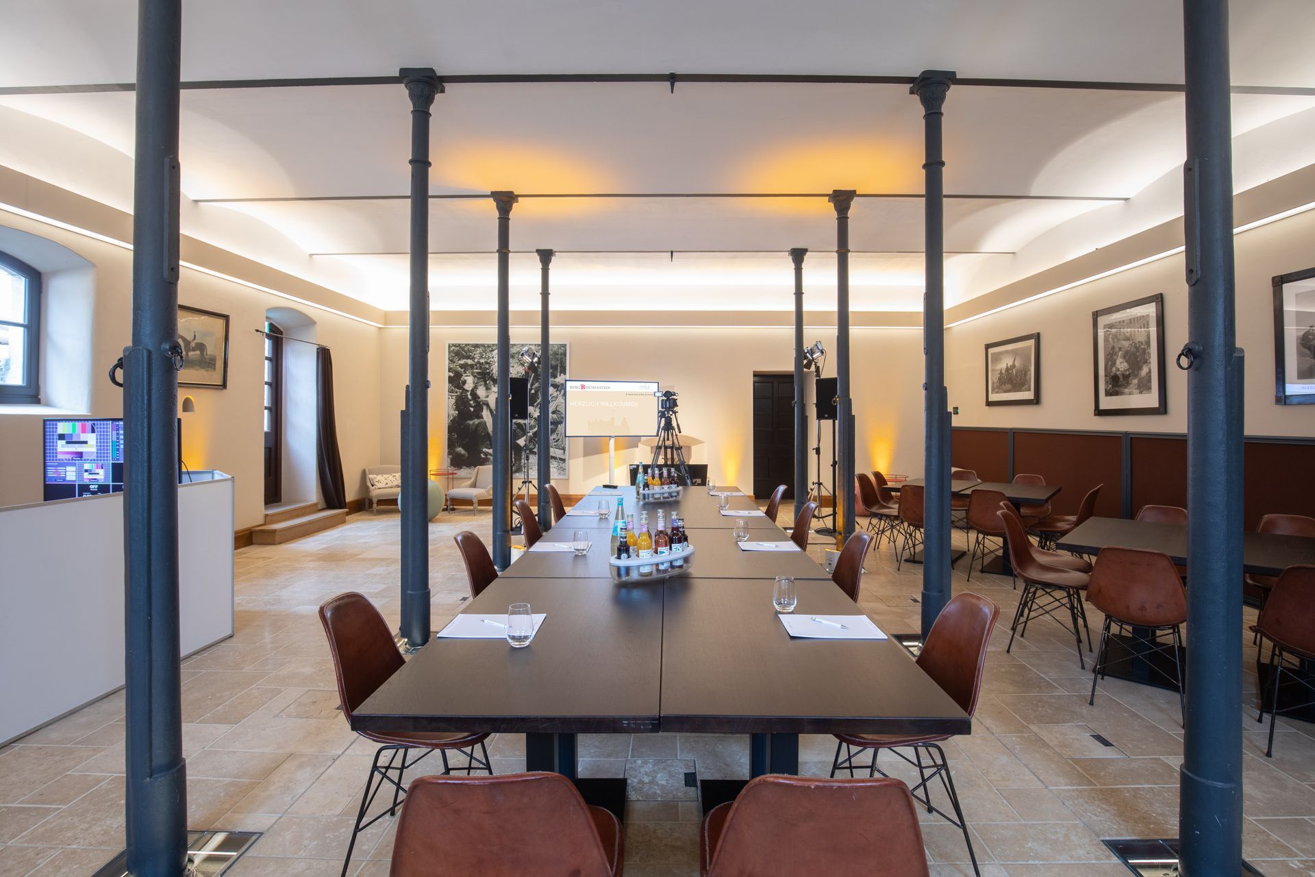 Ein langer, schmaler Konferenzraum verfügt über einen zentralen Holztisch, moderne Stühle, Steinböden und schwarze eiserne Stützpfeiler.