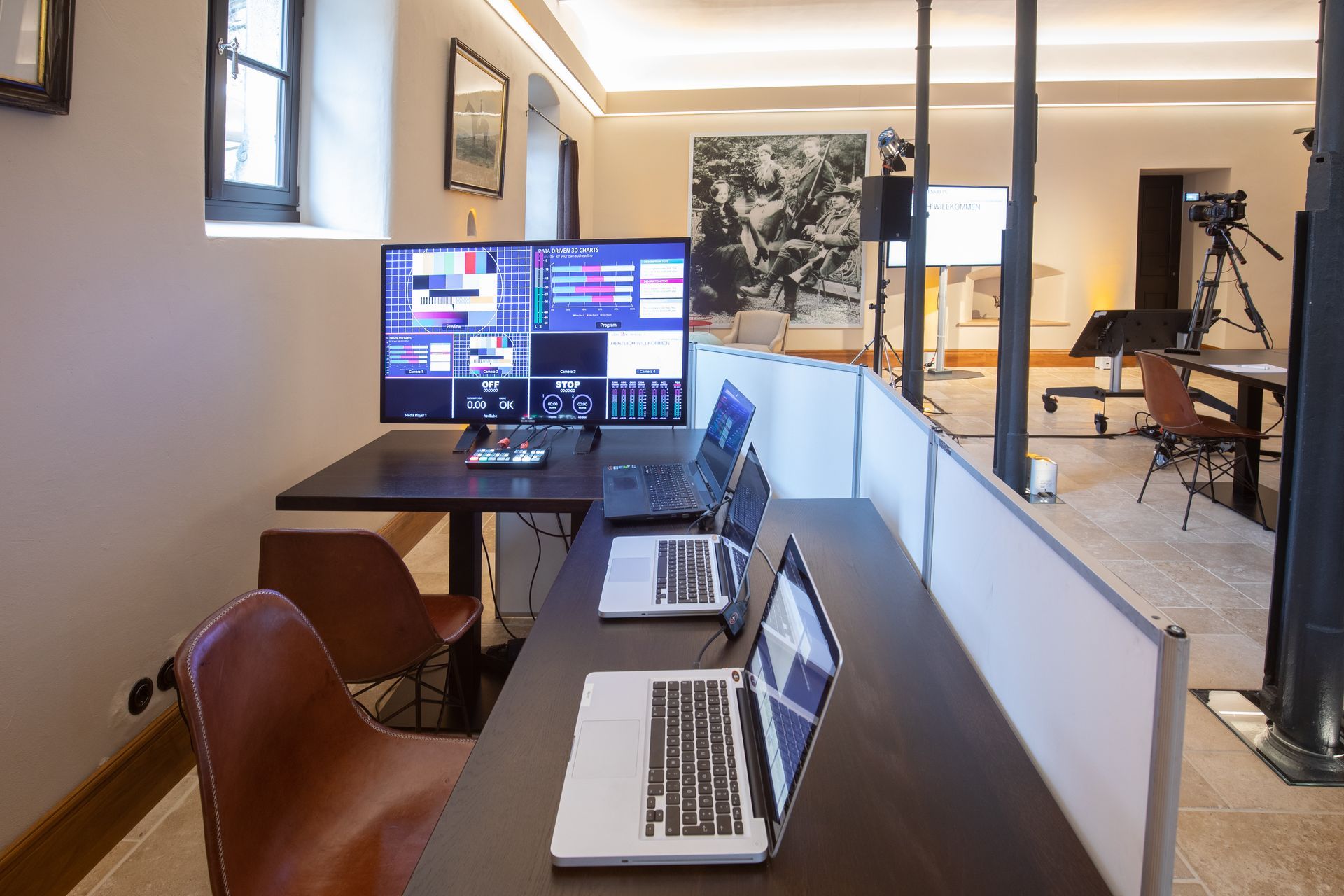 A studio setup featuring a computer monitor, two laptops, and chairs in a brightly lit, minimalist interior.