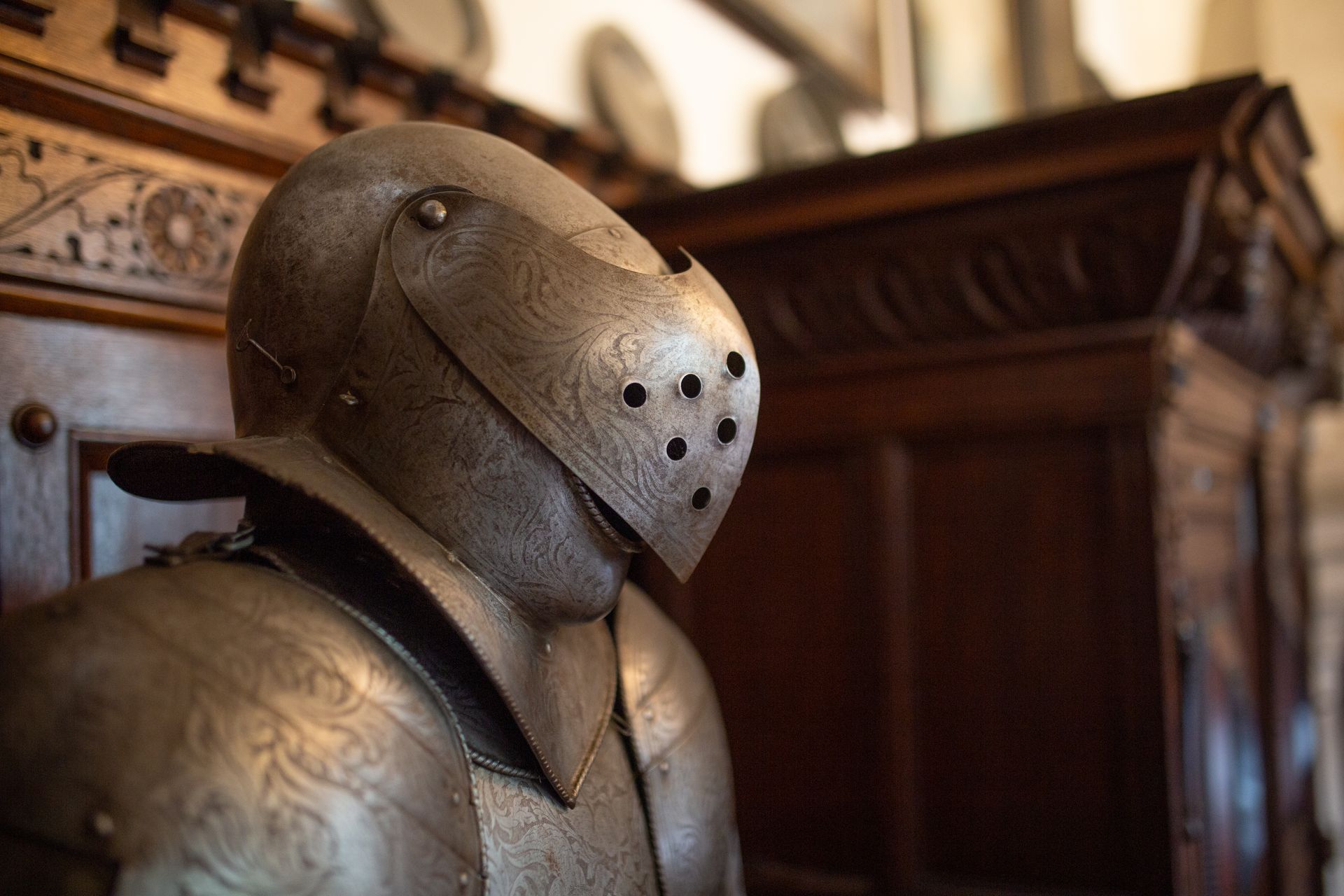 A close-up of a metal suit of armor with a detailed visor against a dark wooden background.