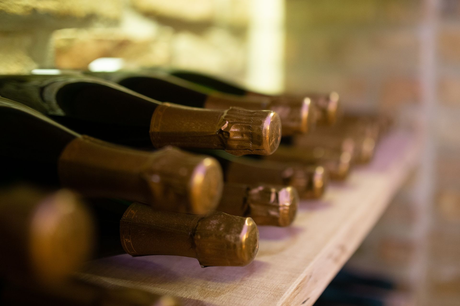 Reihen dunkler Weinflaschen mit kupferfarbenen Verschlüssen stehen auf Holzregalen in einem Steinkeller.