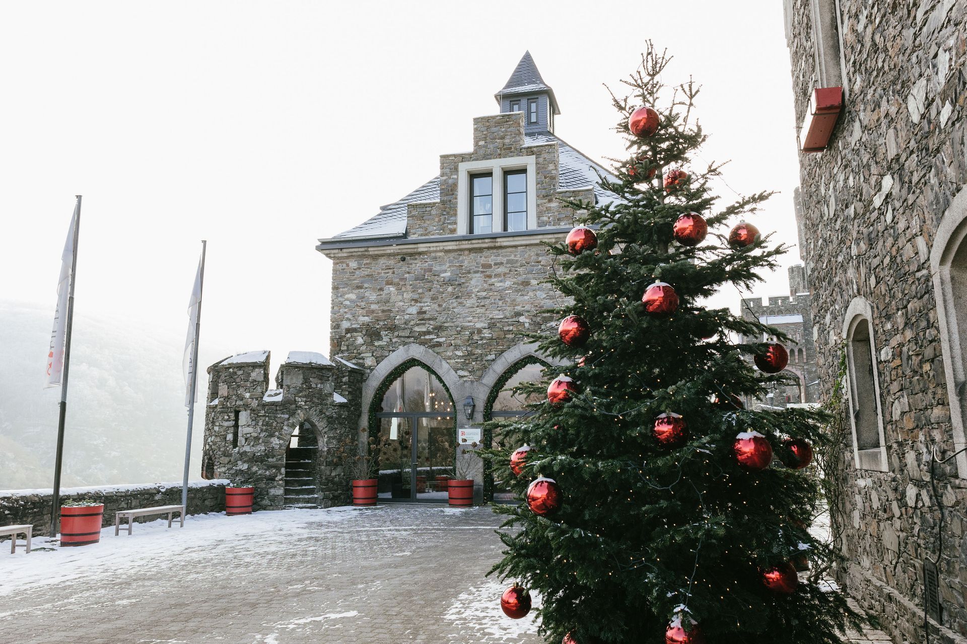 Ein steinerner Burghof im Winter mit einem hohen, geschmückten Weihnachtsbaum mit rotem Schmuck.