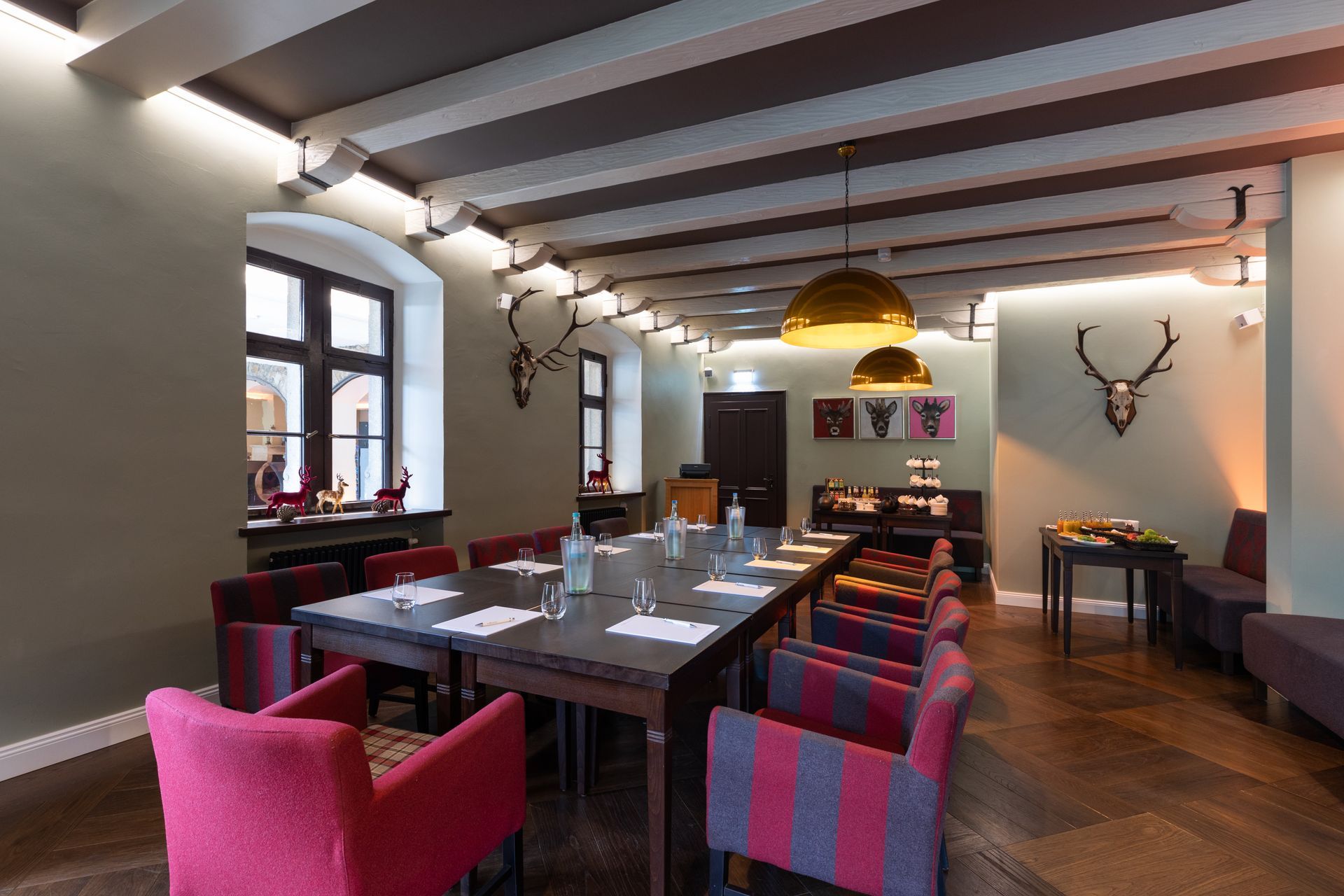 A conference table with chairs in a wood-paneled room decorated with deer antlers and modern lighting.