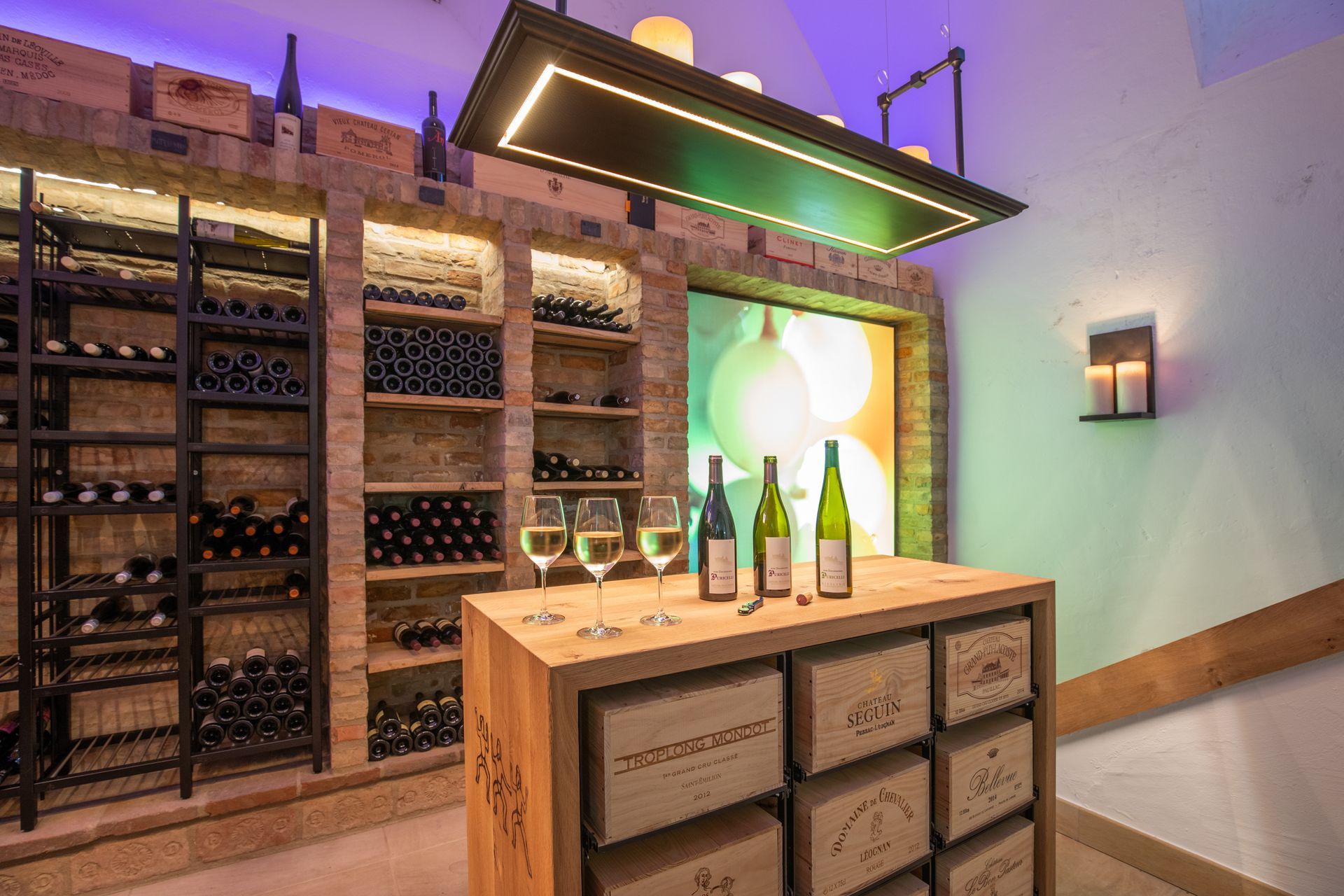 Ein moderner Weinkeller mit gemauerten Regalen, Reihen von Weinflaschen, einem hölzernen Verkostungstisch und stimmungsvoller violetter Beleuchtung.