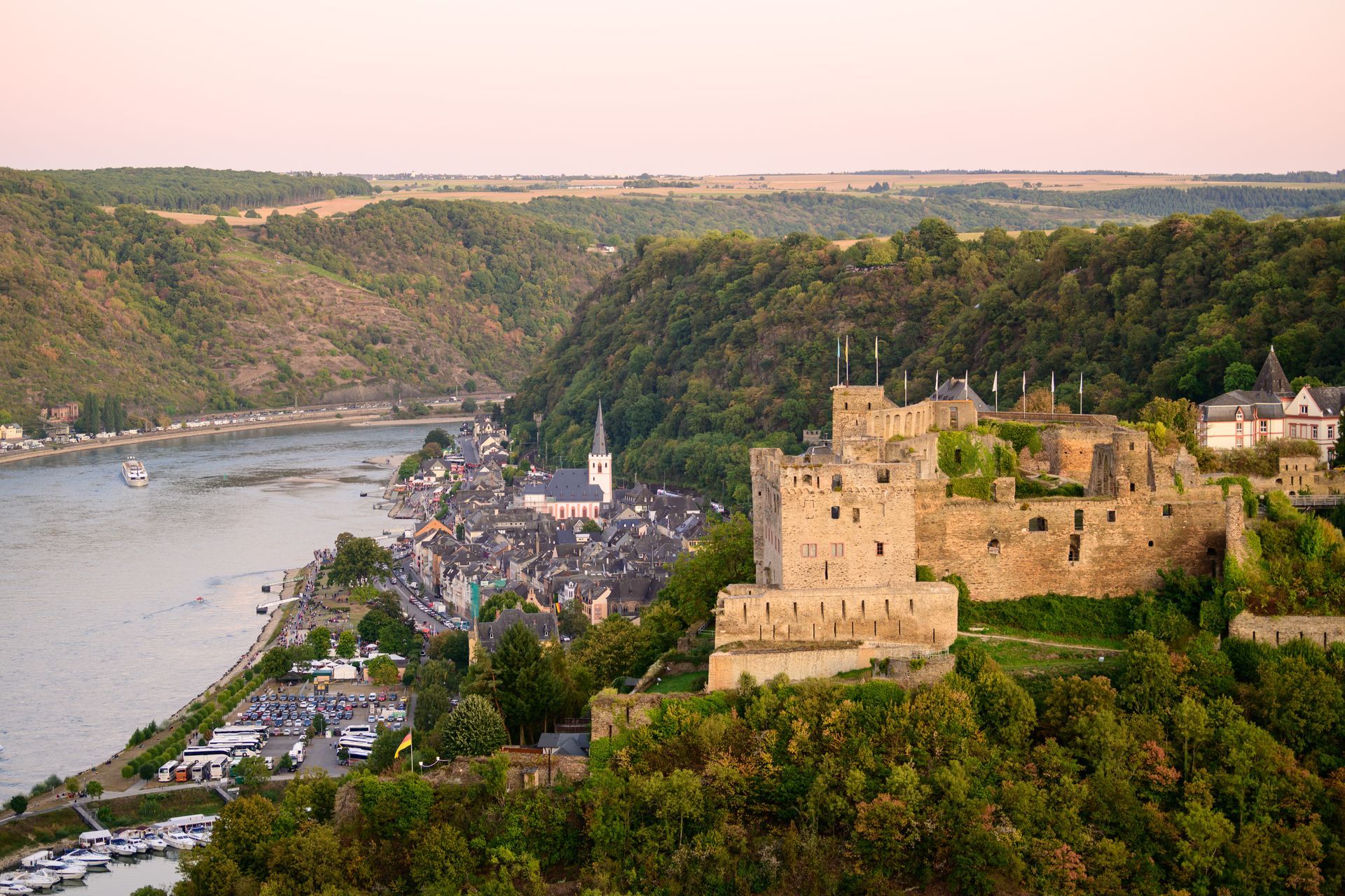 Bei Sonnenuntergang überblickt eine steinerne Burg eine kleine Stadt, die sich an einem gewundenen Fluss schmiegt.