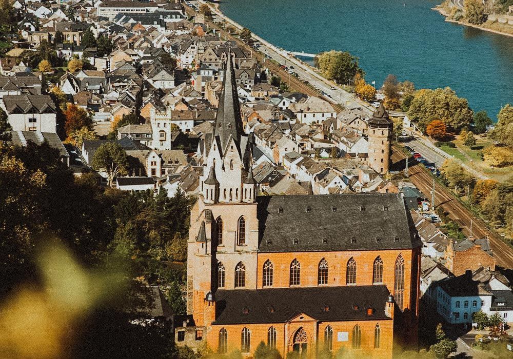 Vogelperspektive auf eine gotische Backsteinkirche mit hohem, spitzem Turm in einer deutschen Stadt an einem Fluss.