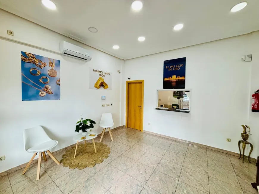 Sala de espera luminosa y minimalista con sillas blancas, una mesa pequeña, obras de arte en la pared y una puerta de madera.