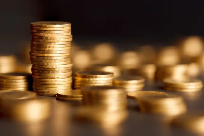 Pila de monedas de oro sobre una mesa con más monedas borrosas al fondo.