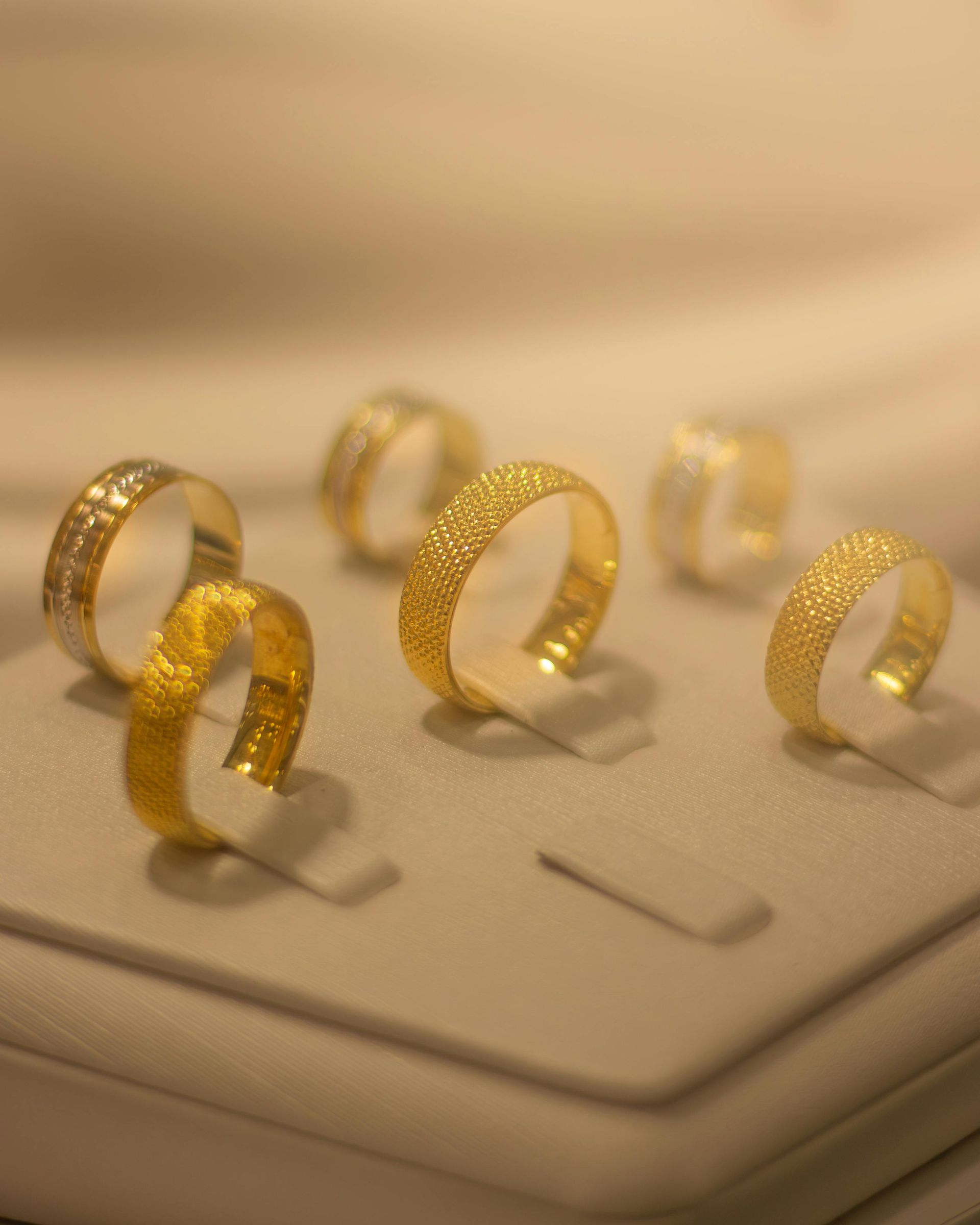 Anillos dorados texturizados expuestos en un soporte de joyería beige bajo una iluminación cálida y suave.