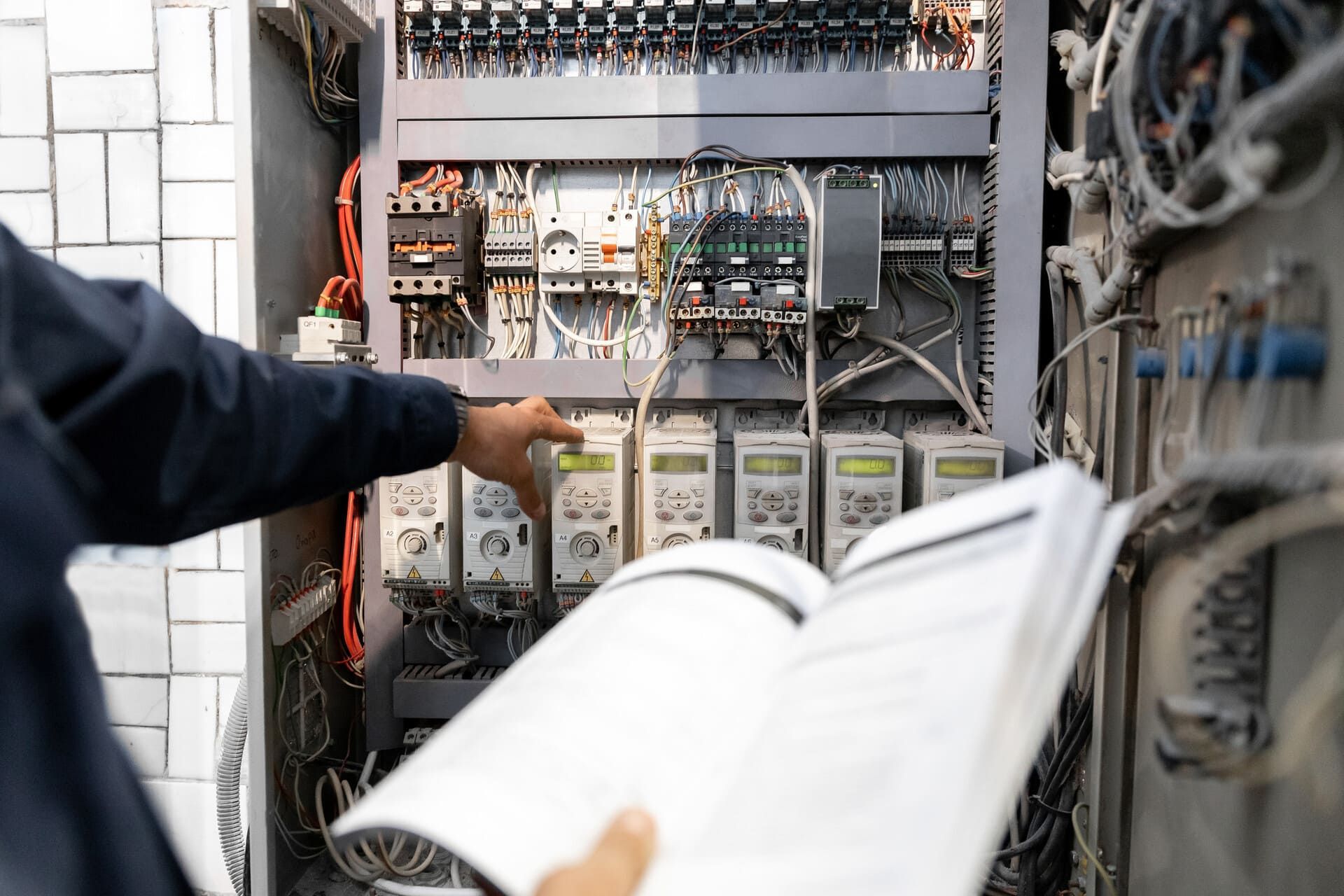 Persona inspeccionando un panel de control eléctrico con un manual en la mano.