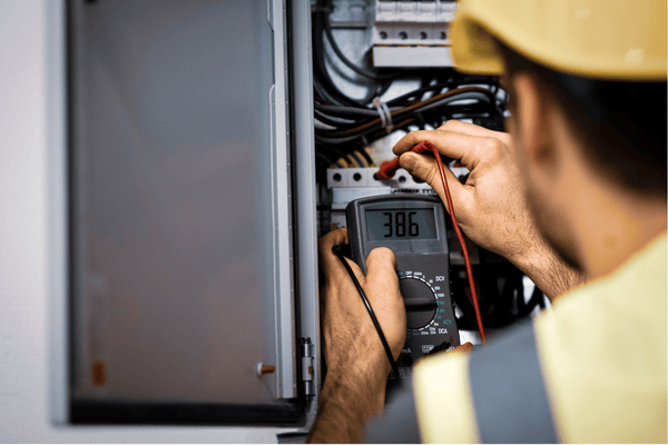 Un electricista con casco utiliza un multímetro dentro de un panel eléctrico para probar el voltaje.