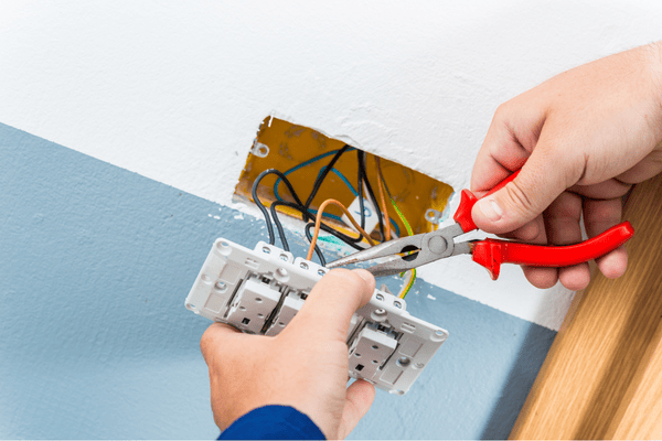 Persona que utiliza alicates para cablear un interruptor de luz en una pared.