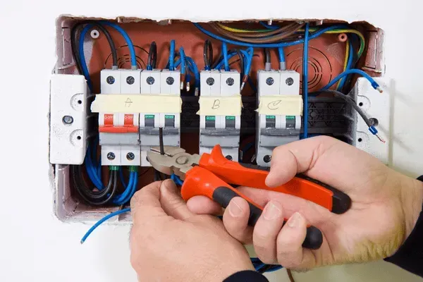 Manos utilizando alicates para trabajar en el cableado eléctrico en una caja de interruptores.