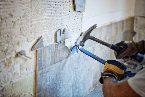 Persona quita azulejos de la pared con un martillo y una palanca.