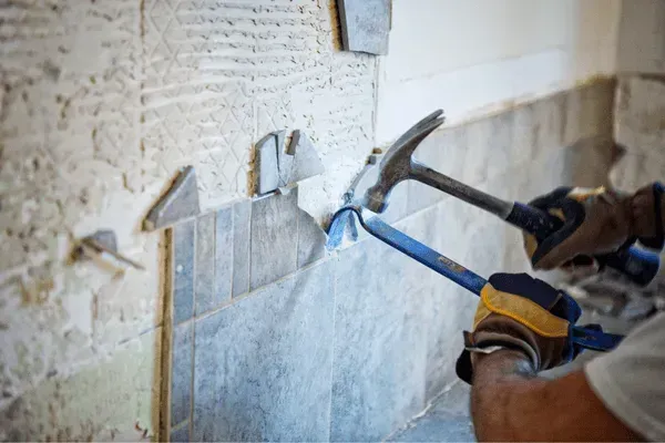 Persona quita azulejos de la pared con un martillo y una palanca.