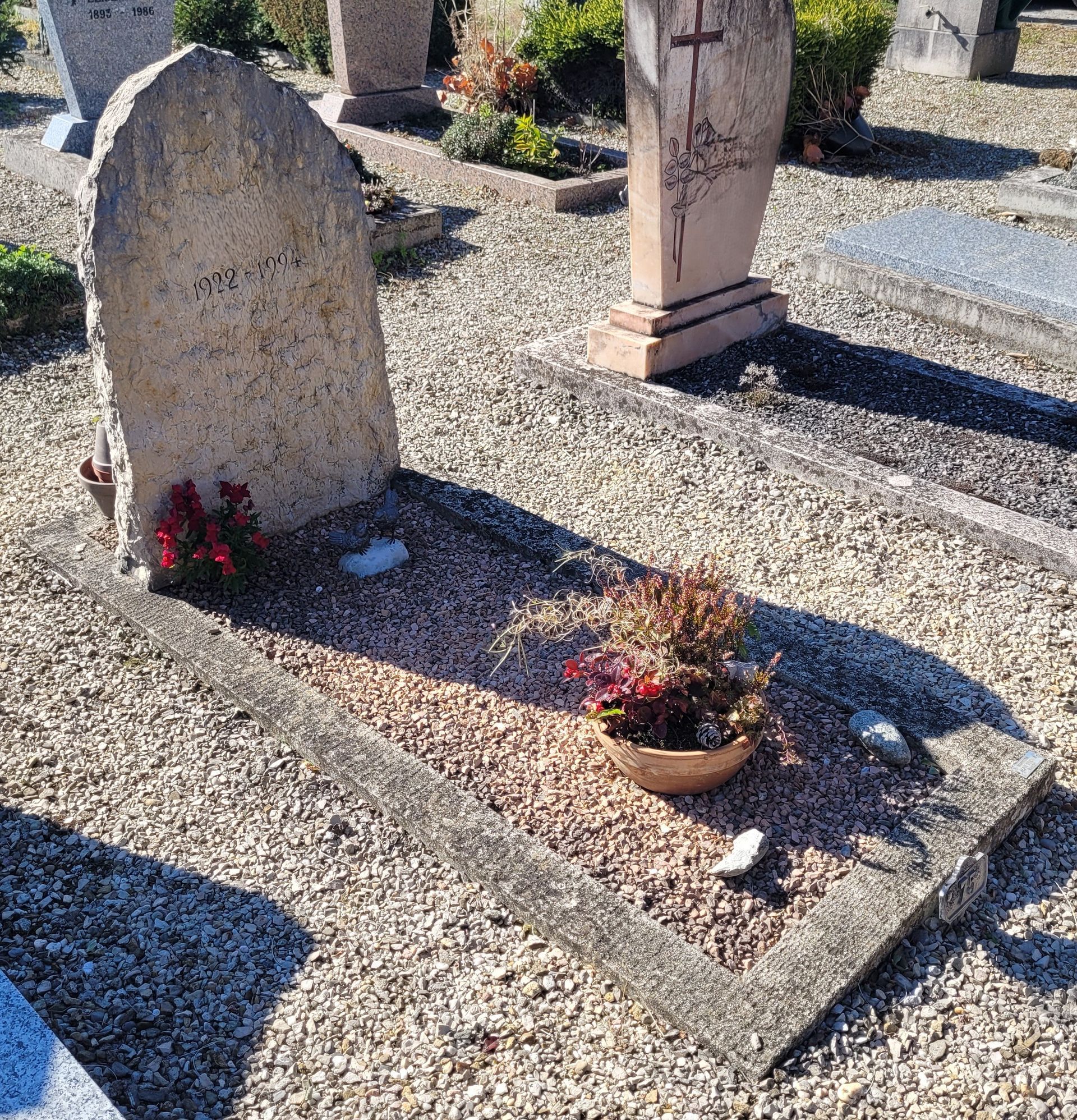 Pierre tombale en granit bleu dans un cimetière herbeux, avec une stèle surélevée.