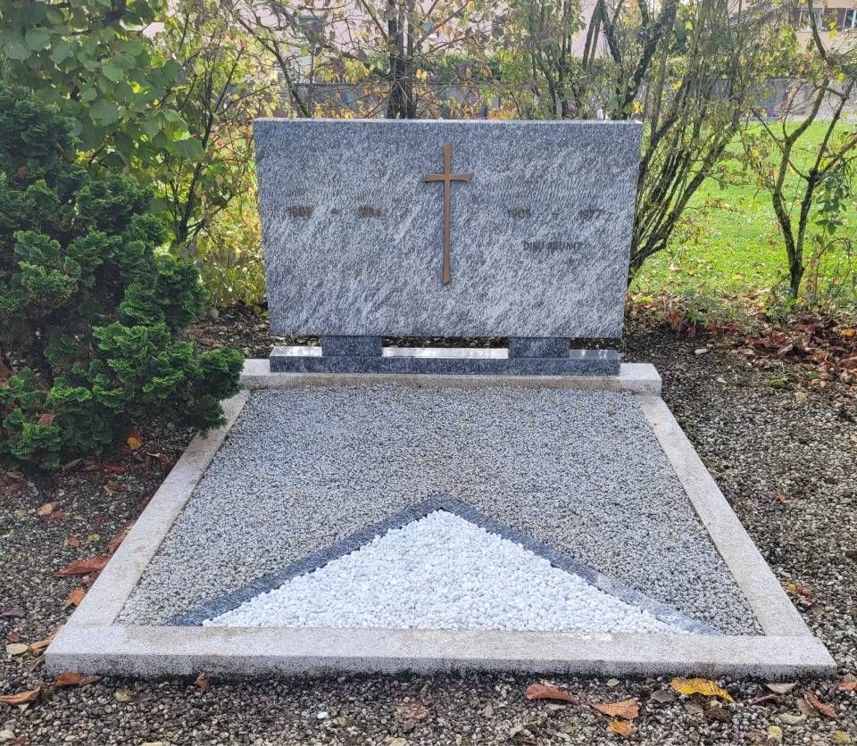 Monument funéraire en granit avec croix dorée et gravier blanc, situé dans un jardin