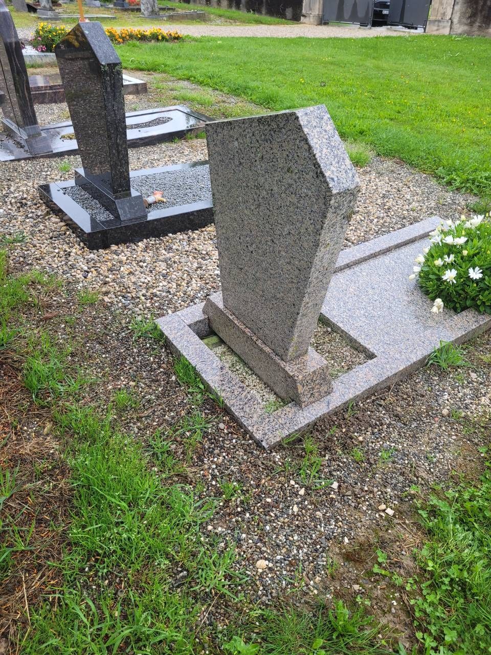 Deux pierres tombales grises sur une parcelle de cimetière herbeuse,