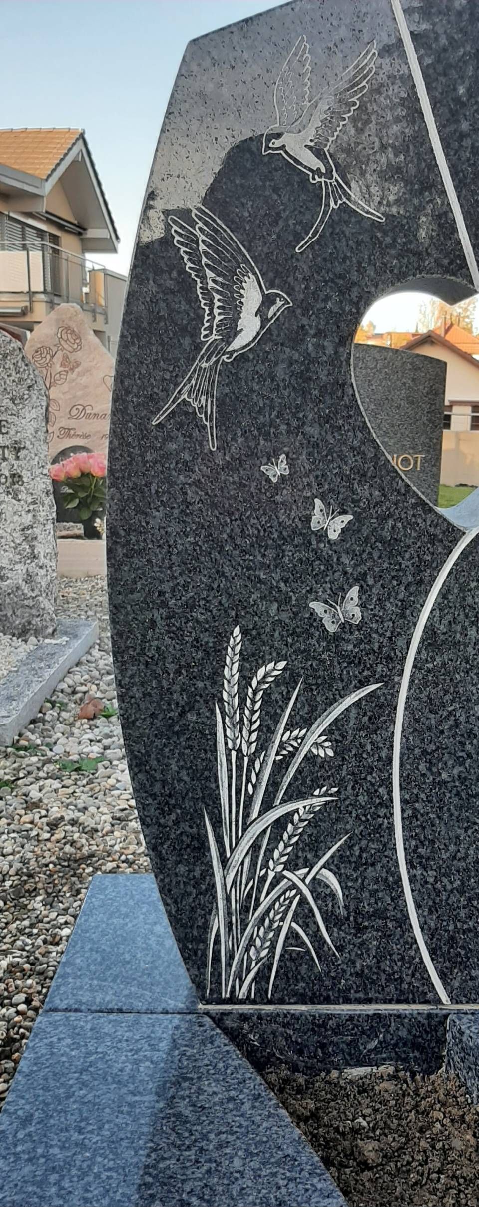 Pierre tombale commémorative en granit noir avec motif floral gravé et découpe en arc de cercle dans un cimetière