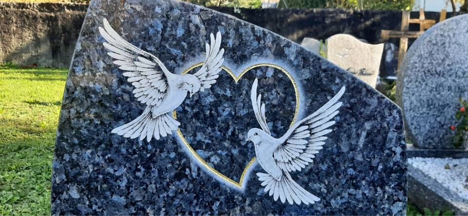 Pierre tombale en granit gris ornée de deux colombes blanches et d'un ruban gravés sur le devant