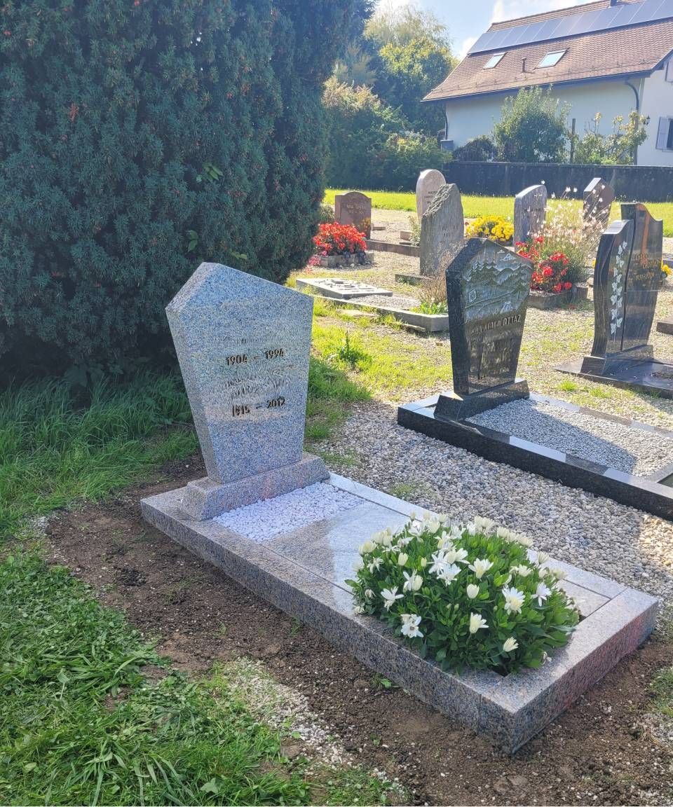Pierre tombale en granit ornée de fleurs blanches dans un cimetière ensoleillé