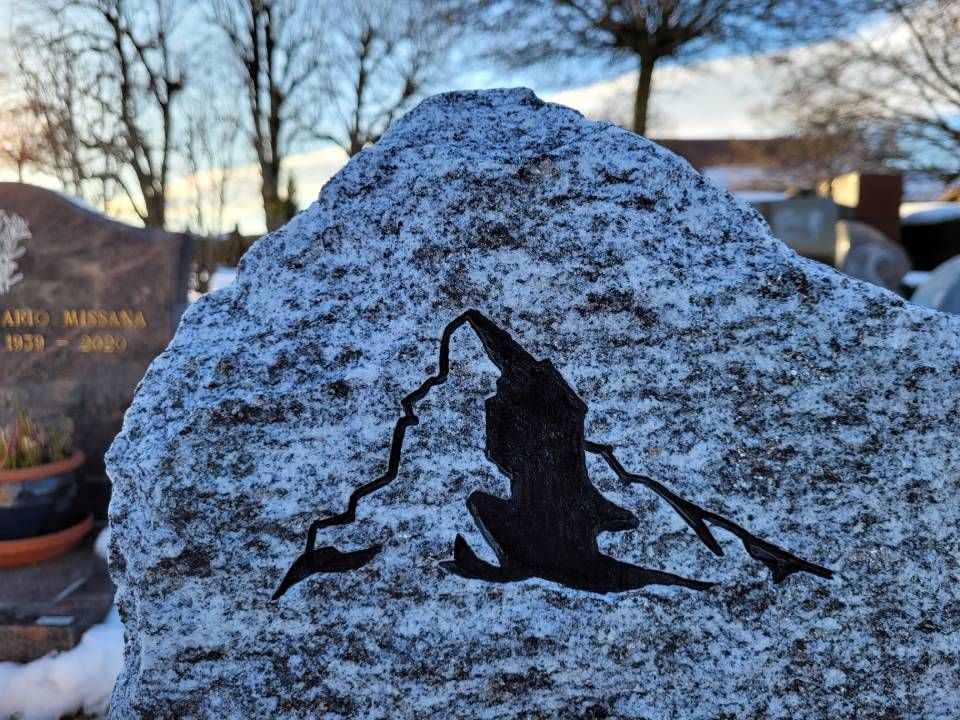 Pierre tombale grise saupoudrée de neige, avec la silhouette d'une montagne noire, dans un cimetière au coucher du soleil