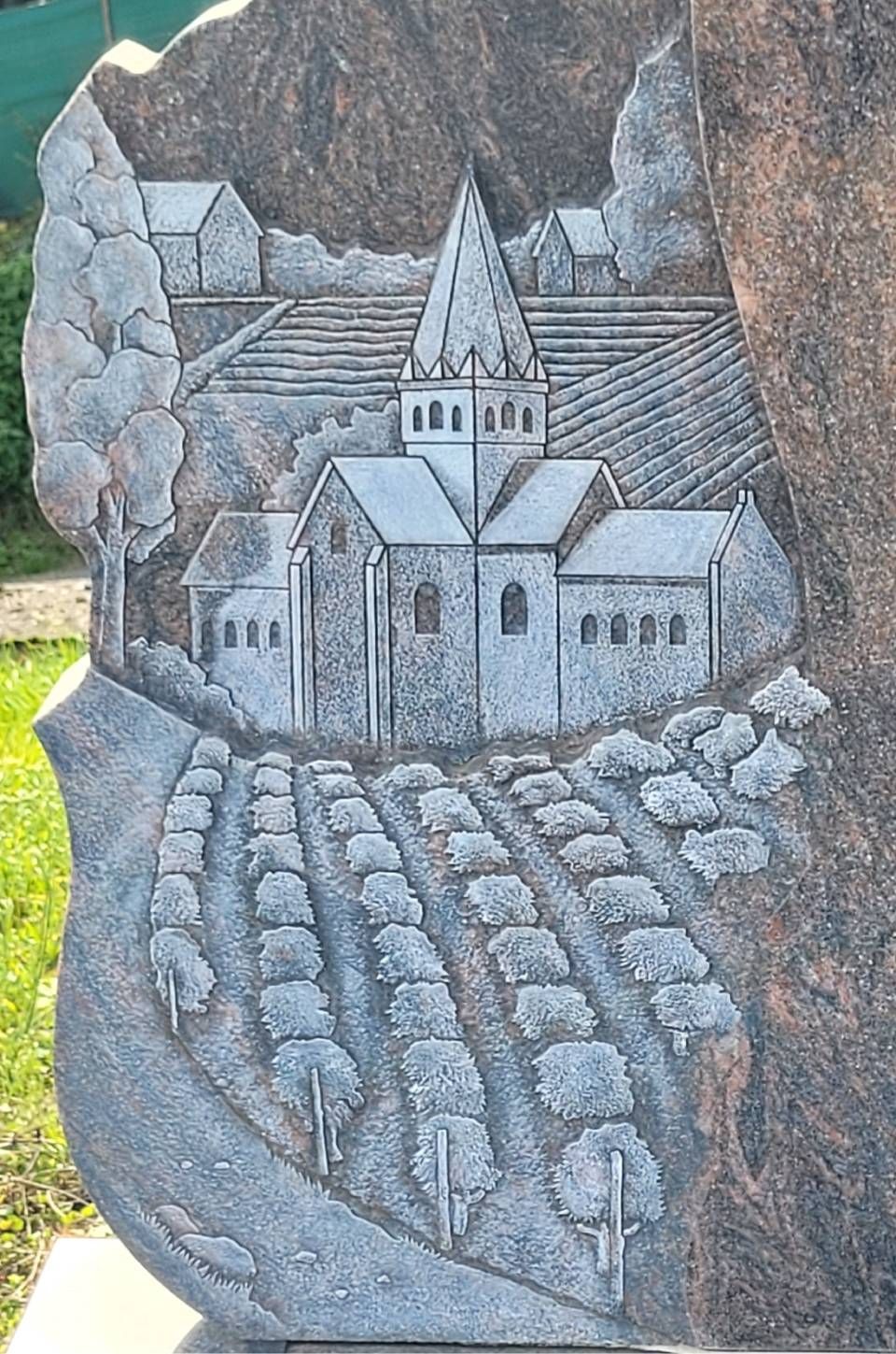 Sculpture en pierre d'une église avec un haut clocher, des montagnes et des rangées de cultures