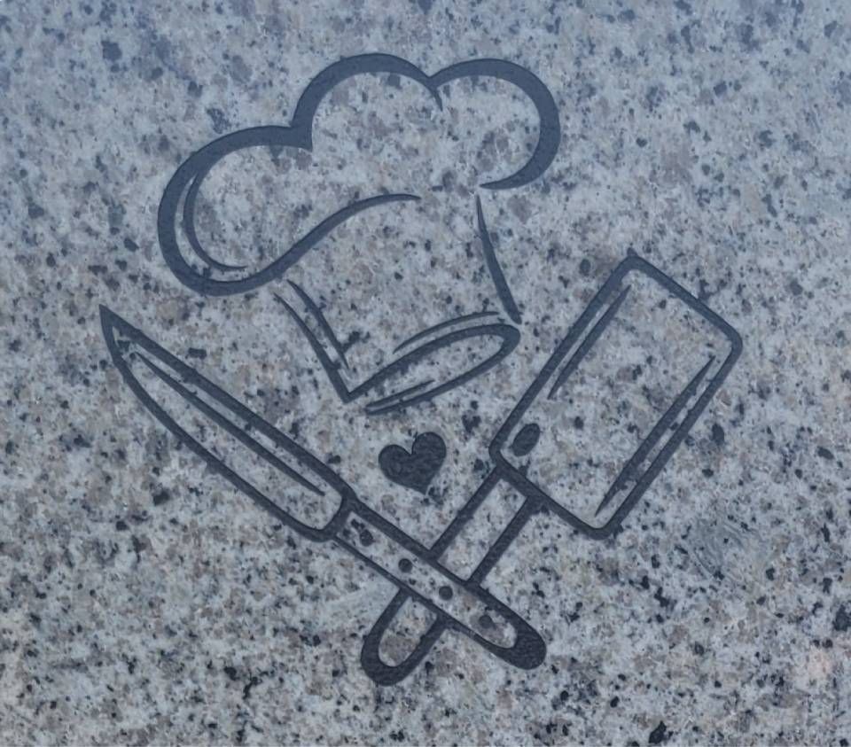 Toque de chef, rouleau à pâtisserie, couteau et couperet ornés d'un petit cœur sur une pierre mouchetée.