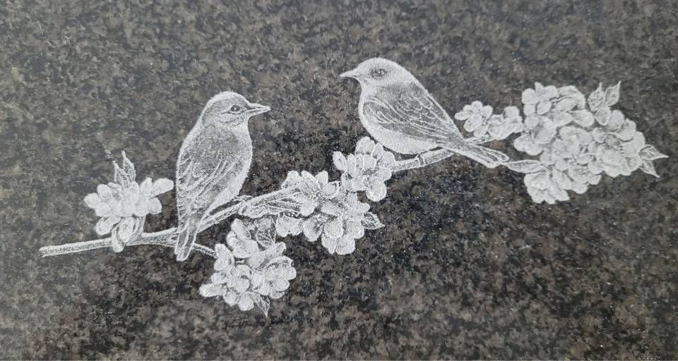 Deux oiseaux perchés sur une branche fleurie, dessinés en blanc sur une pierre sombre