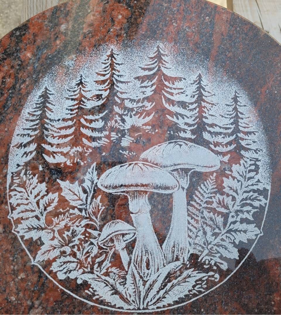 Champignons blancs et fougères dans un décor forestier, gravés sur une plaque de pierre circulaire.