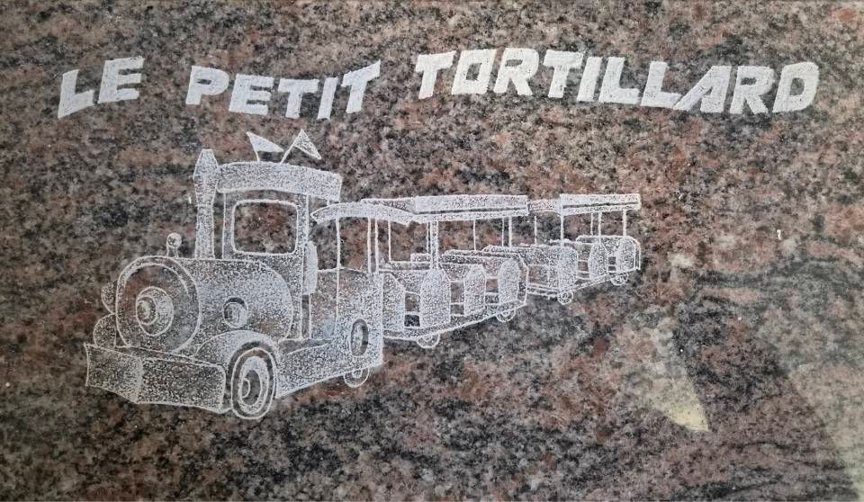 Enseigne « Le Petit Tortillard » avec une illustration de train vintage blanche sur un mur de pierre mouchetée