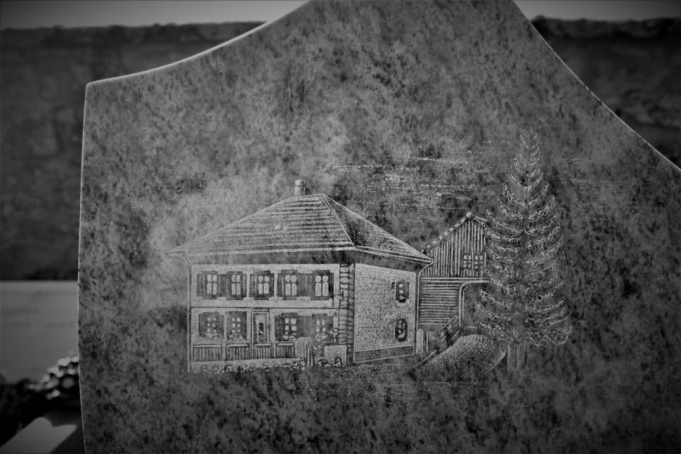 Pierre tombale gravée d'une maison dans une scène de cimetière en noir et blanc brumeuse