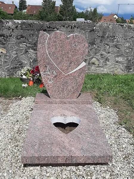 Pierre commémorative rose en forme de cœur avec un cœur blanc incrusté, placée à l'extérieur près d'un muret et de fleurs