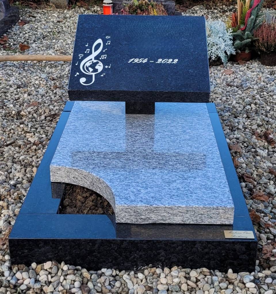 Banc commémoratif en granit bleu orné d'une gravure en forme de clé de sol, dans un jardin de galets.