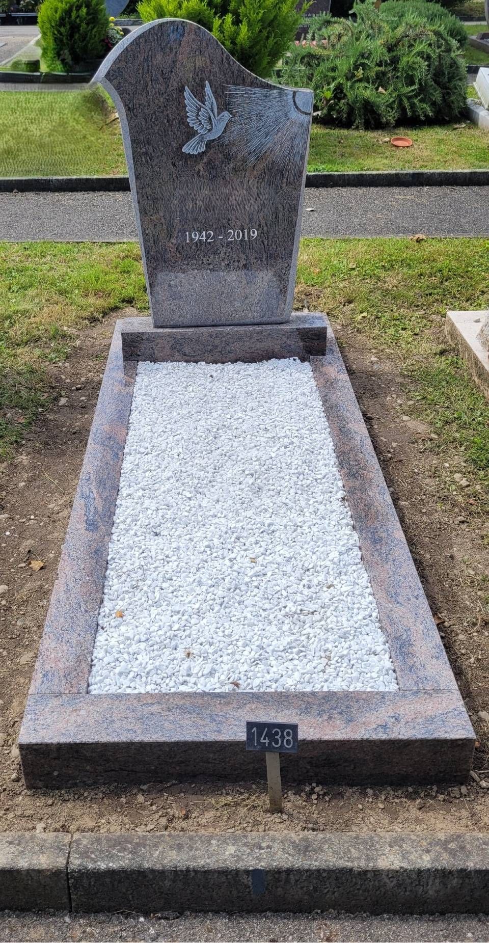 Pierre tombale avec stèle grise et bordure de gravier blanc dans un cimetière