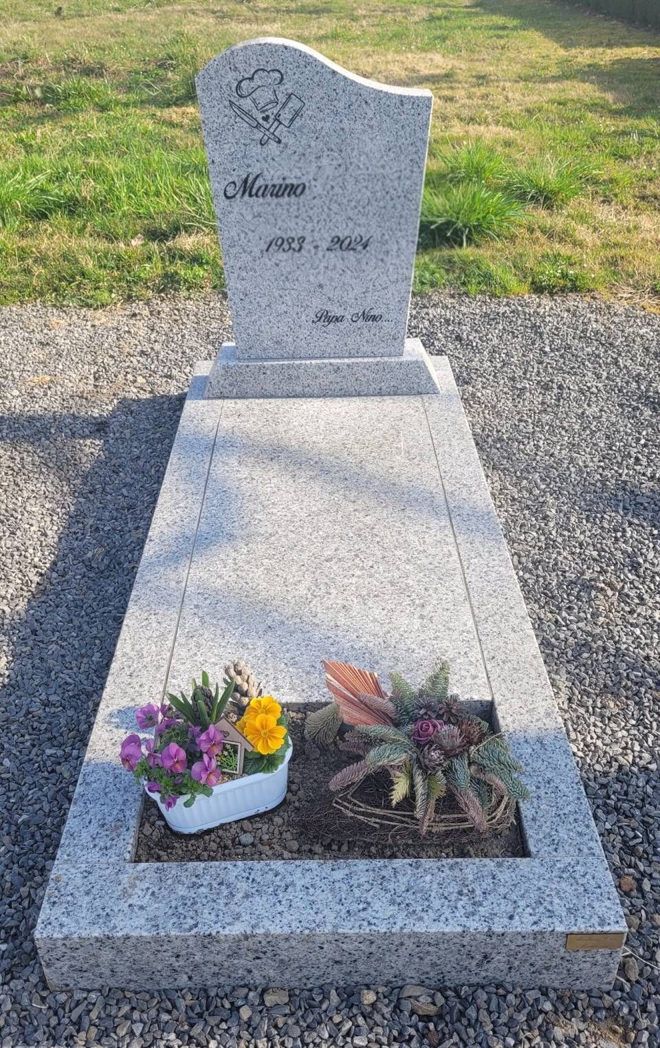 Pierre tombale fleurie sur un chemin de gravier dans un cimetière herbeux