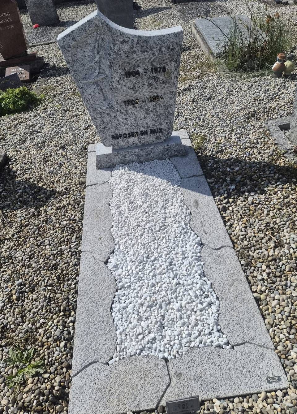 Pierre tombale avec dalle de béton fissurée dans une parcelle de cimetière gravillonnée