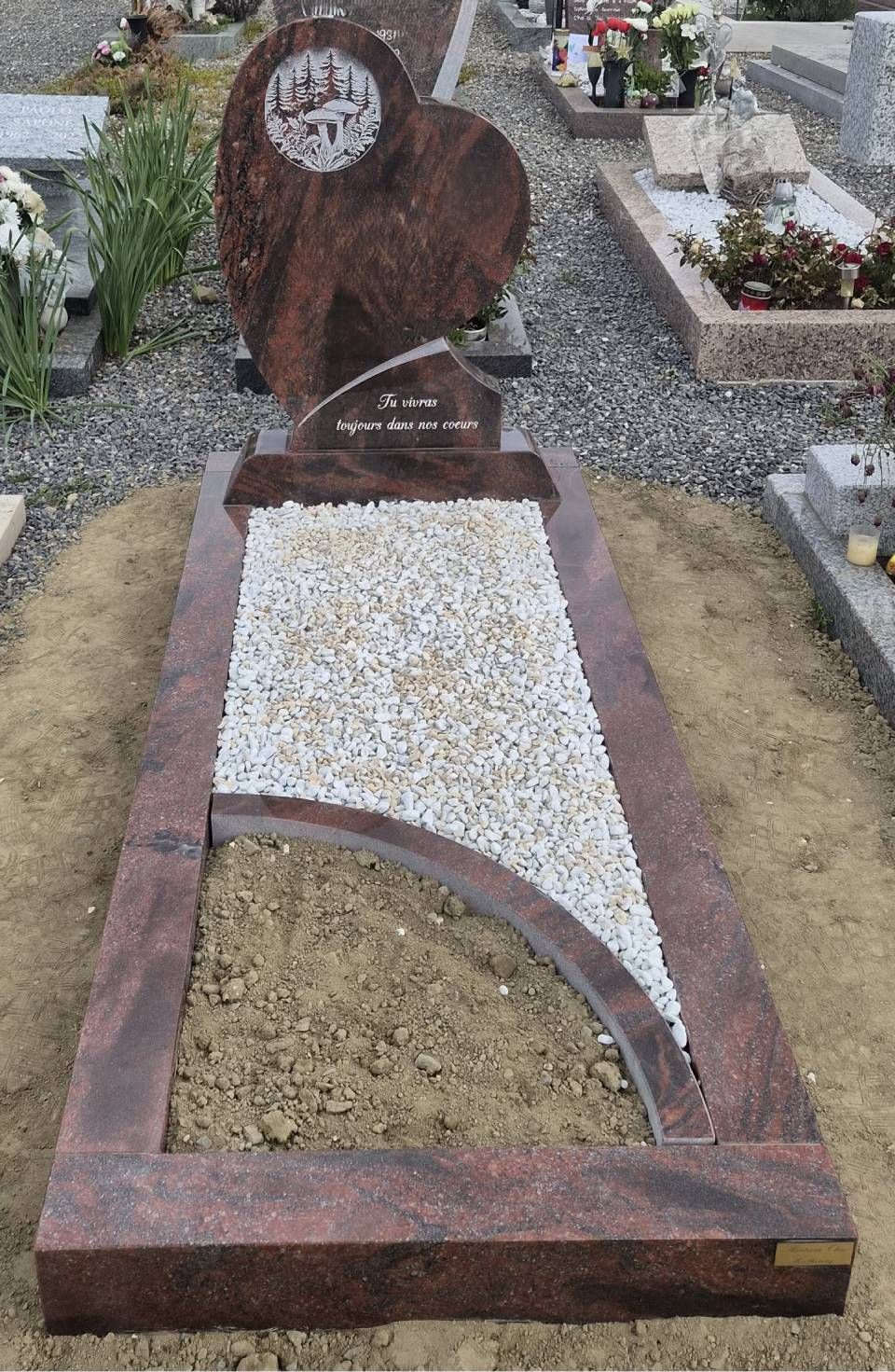 Pierre tombale avec une croix rouillée et du gravier blanc incrusté dans une parcelle de cimetière