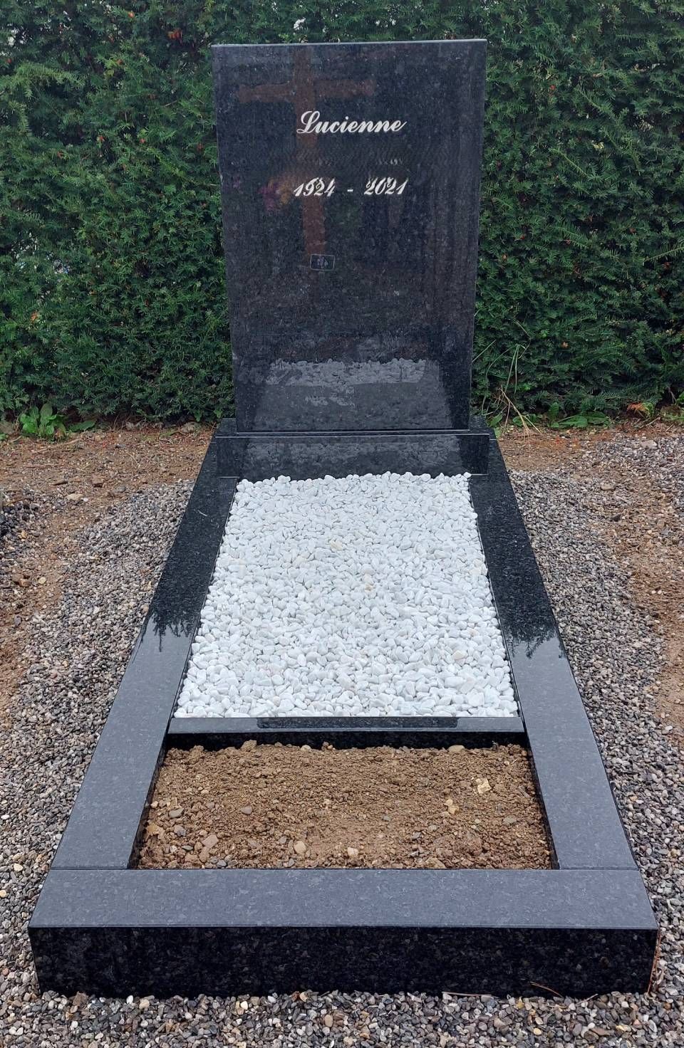 Pierre tombale avec stèle sombre et lit de gravier blanc dans un cimetière paysager