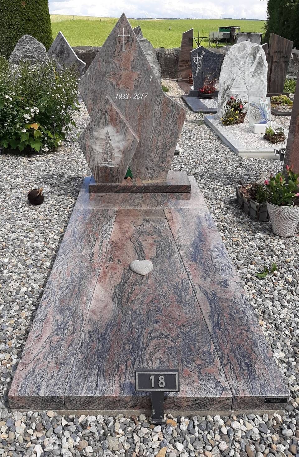 Pierre tombale en granit avec stèle triangulaire et base plate dans un cimetière, marquée 18