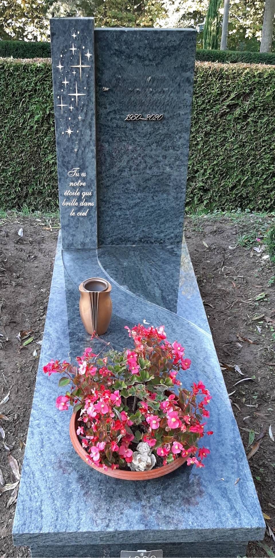 Pierre tombale commémorative avec un pot de fleurs et une petite bougie à sa base, dans un cadre de jardin