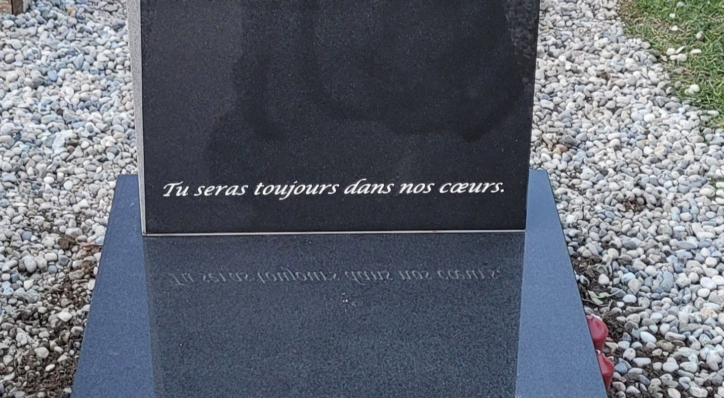 Gros plan sur une plaque commémorative en granit sombre avec un texte français gravé, posée sur un sol de gravier.