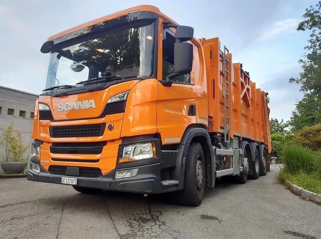 Un gros camion poubelle orange est garé sur le bord d'une route.
