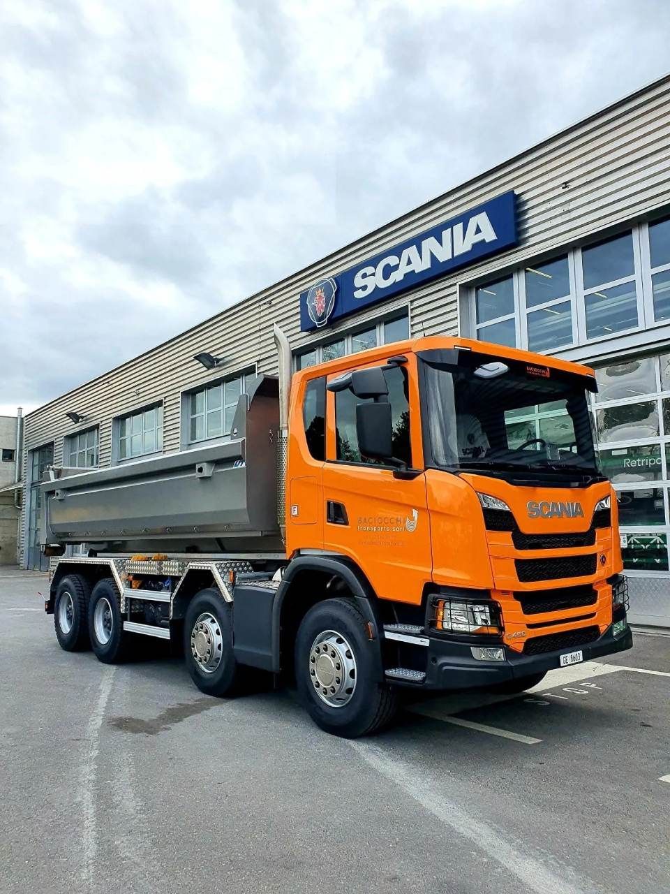 Un camion-benne orange est garé devant un bâtiment Scania.