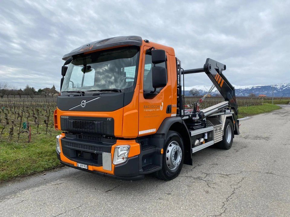 Un camion-benne orange est garé sur le bord d'une route.